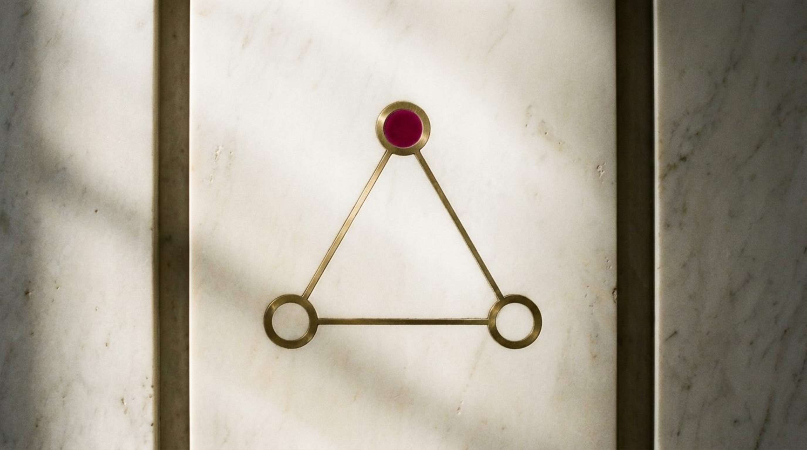 The Ratio mark: a brass triangle inlaid in pale marble, the conclusion node in magenta enamel